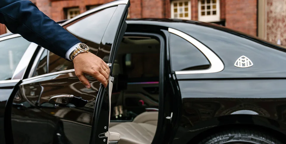 Chauffeur opening the rear door of a black Mercedes-Maybach